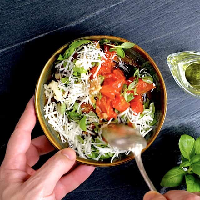 Ingredients to make bruschetta topping being mixed in a bowl with a spoon.
