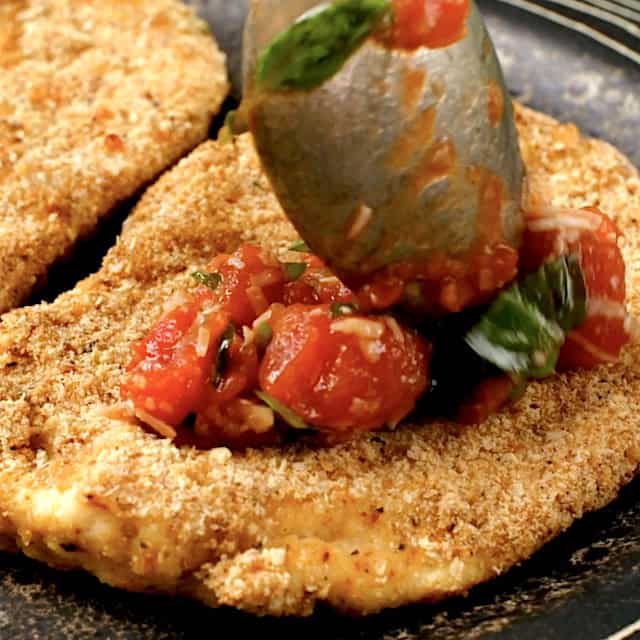Parmesan crusted chicken being topped with bruschetta before serving.