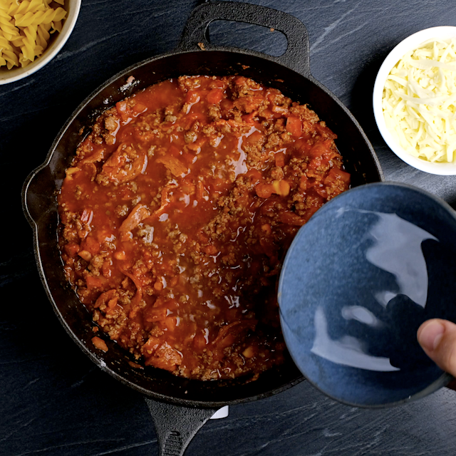 Water being added to pizza pasta sauce mixture in a oven-proof skillet.