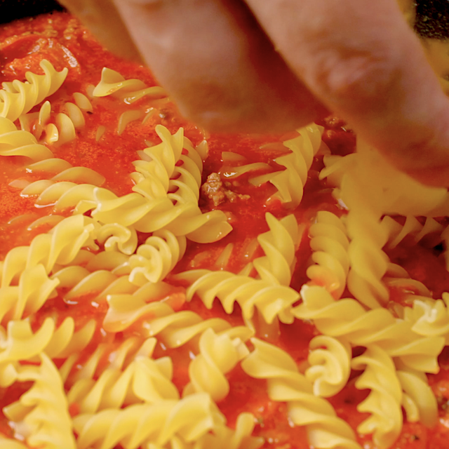 Uncooked pasta being added to pizza pasta sauce in a pot.