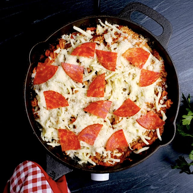 Skillet with pizza pasta topped with cheese and pepperoni, ready to be broiled in the oven.