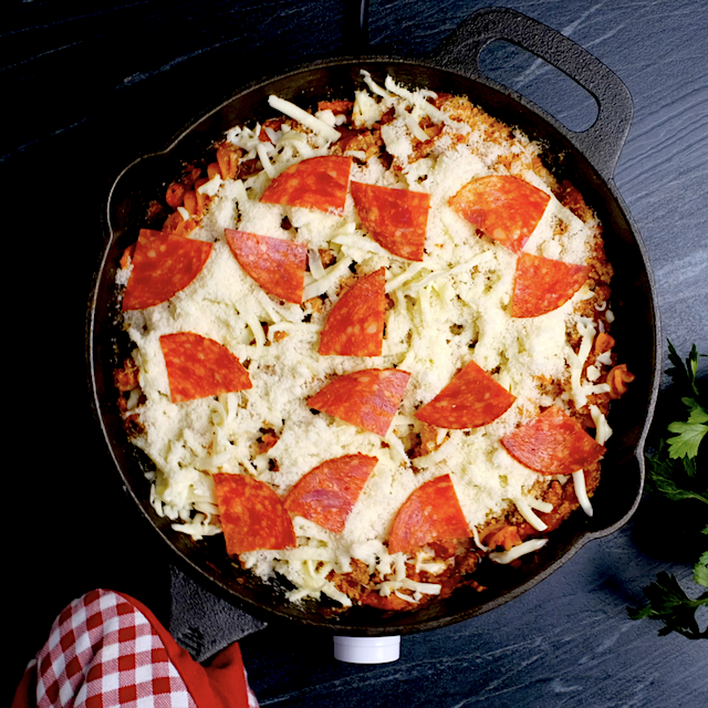 Skillet with pizza pasta topped with cheese and pepperoni, ready to be broiled in the oven.