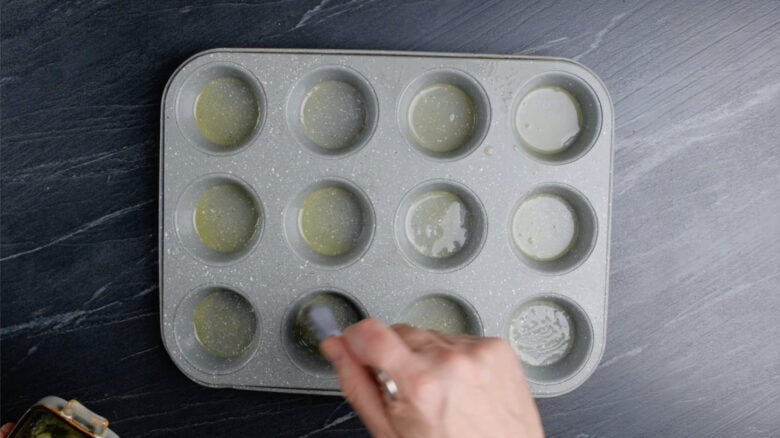 Popover tin being brushed with melted butter.