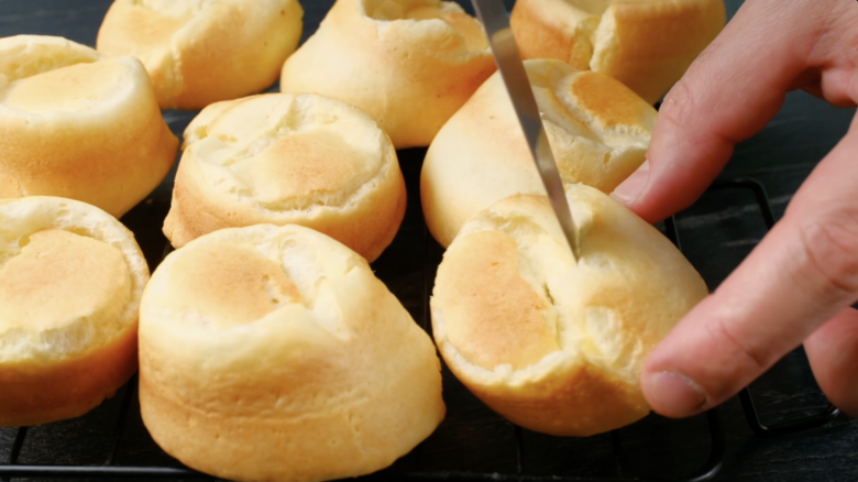 Freshly baked popovers being pierced at the bottom with a small knife. 