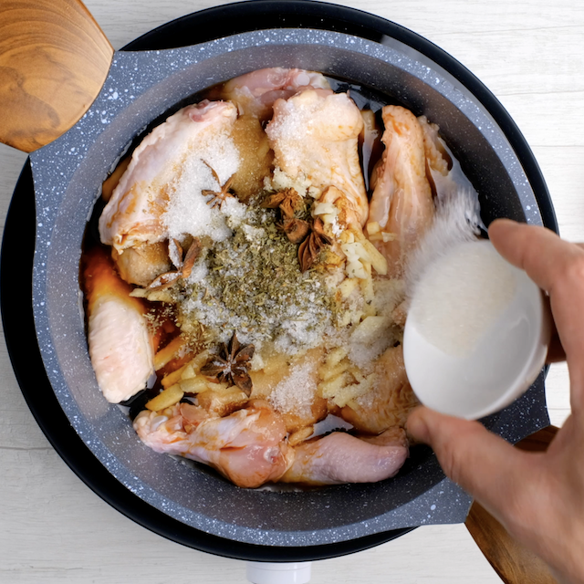 Spices and ingredients being added to a pot with chicken wings to make braised Asian chicken wings at home.