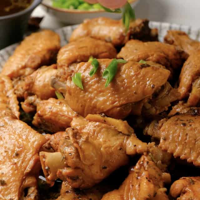 Chopped green onions being sprinkled on top of freshly cooked Asian chicken wings.