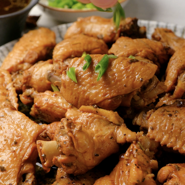 Chopped green onions being sprinkled on top of freshly cooked Asian chicken wings.