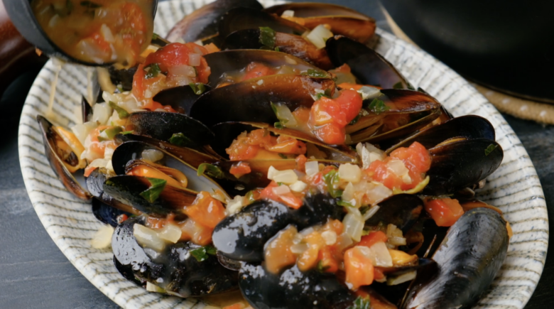 White wine sauce being poured on top for cooked mussels.