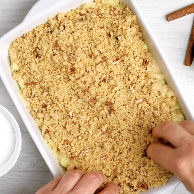 Streusel topping added on top of apple coffee cake batter in a pan.