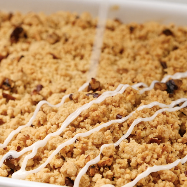 Icing being drizzle on freshly baked apple coffee cake.