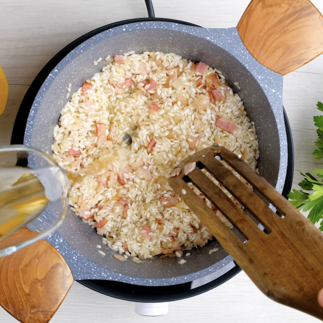 White wine being poured into butternut squash risotto pot.