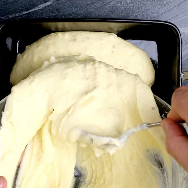 Creamy mashed potato mixture being transferred into a baking dish.