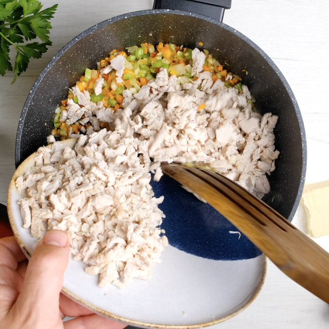 Shredded turkey being added to sauteed vegetables to make turkey bolognese.
