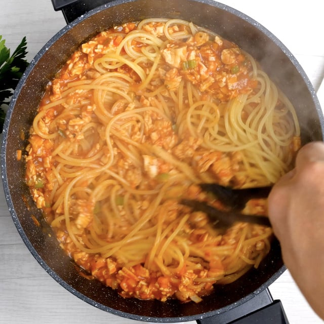Cooked spaghetti being mixed into turkey bolognese meat mixture.