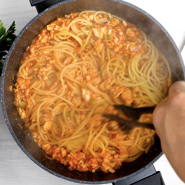 Cooked spaghetti being mixed into turkey bolognese meat mixture.