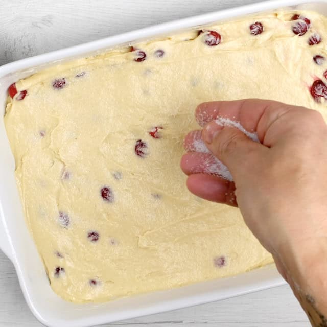 Coarse sugar being sprinkled on top of cranberry cake batter before baking.