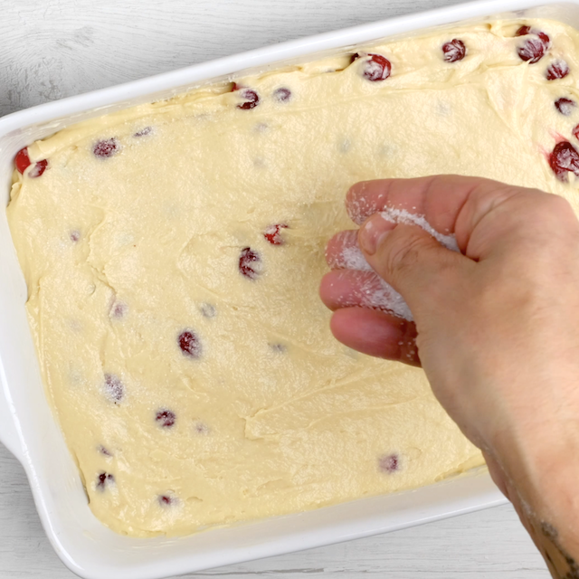 Coarse sugar being sprinkled on top of cranberry cake batter before baking.