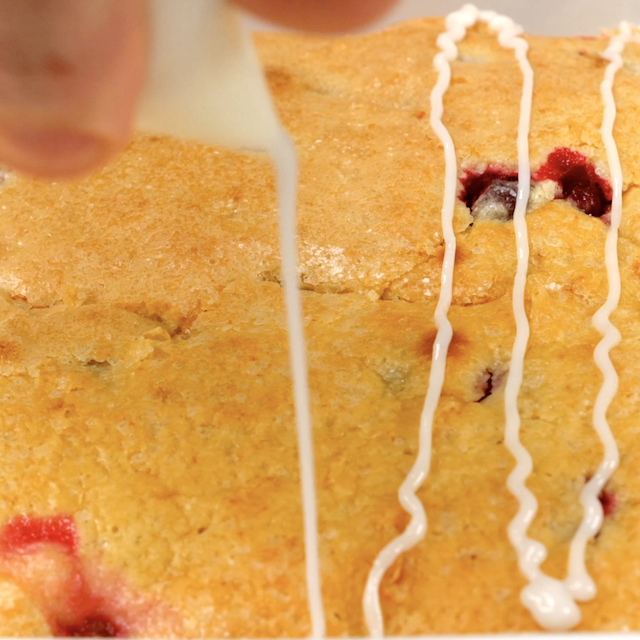 Icing being drizzled on top of freshly baked cranberry cake.