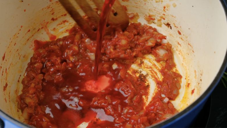 Wine being poured into a Dutch oven with a tomato paste mixture in it.