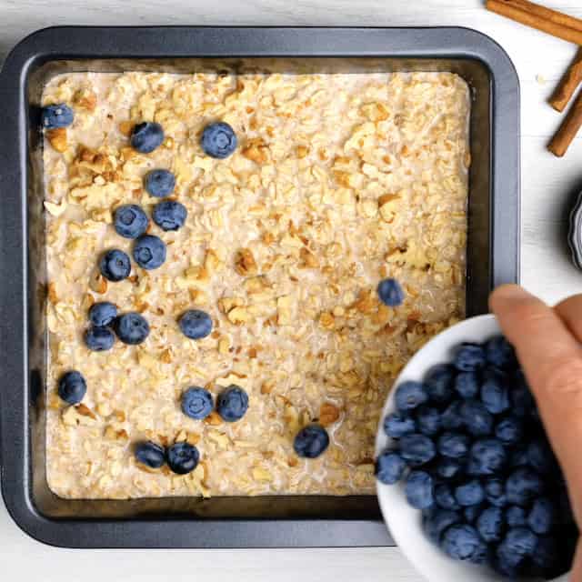 Blueberries being sprinkled on top of oatmeal batter in a pan to make baked blueberry oatmeal.