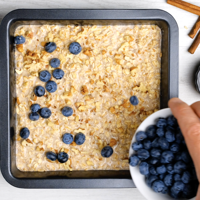 Blueberries being sprinkled on top of oatmeal batter in a pan to make baked blueberry oatmeal.