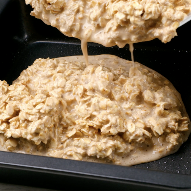 Baked blueberry oatmeal batter being poured into a greased pan.