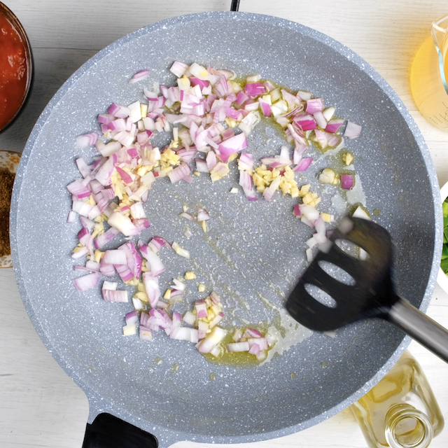 Onion and garlic being sautéed in a pan.