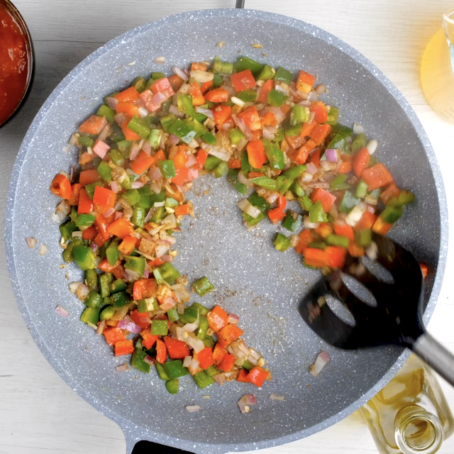 Bell peppers and aromatics being cooked in a pan to make chicken fajita pasta.