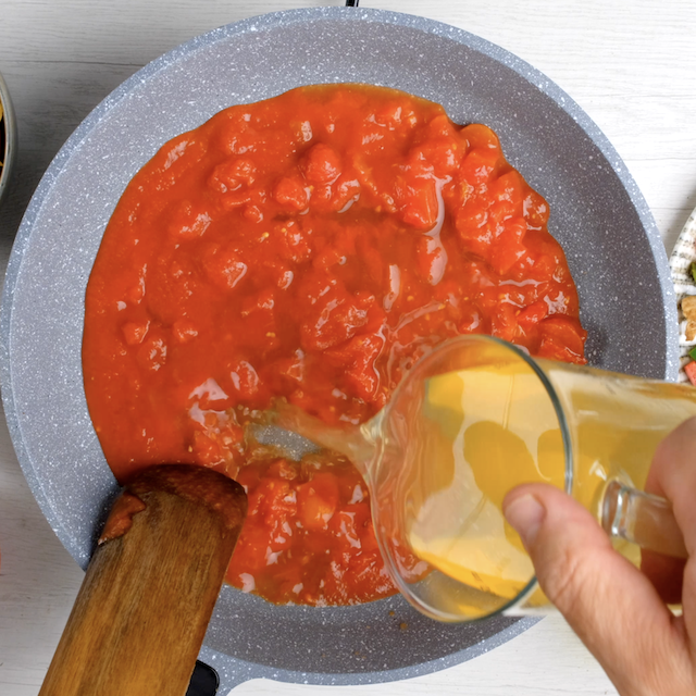 Broth being added to a pot with tomatoes to make chicken fajita pasta.