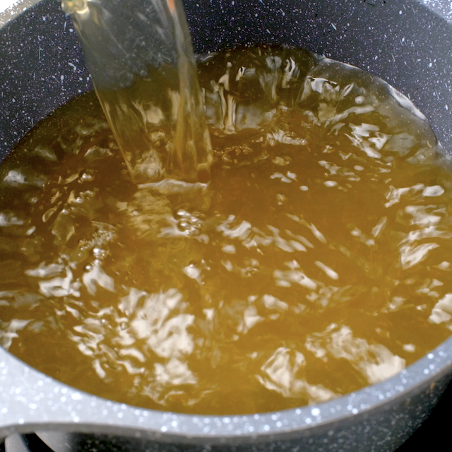 Clam juice being combined with chicken broth to make easy seafood paella at home.