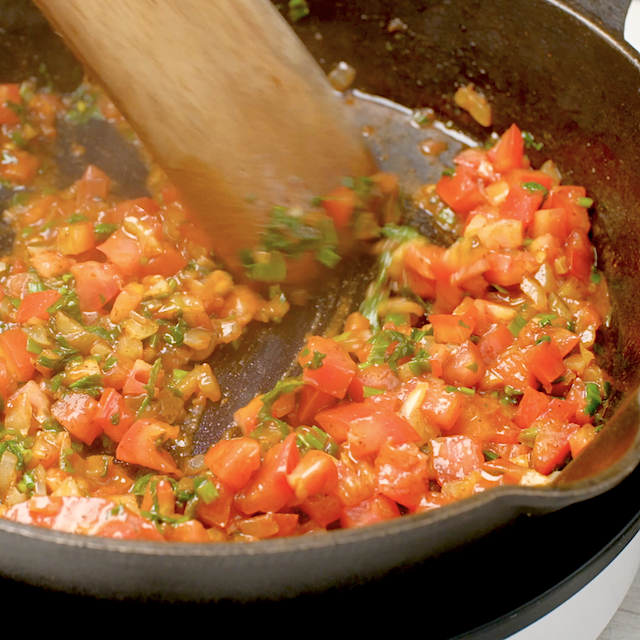 Tomatoes being cooked along with basil, cilantro, and scallions to make easy seafood paella.