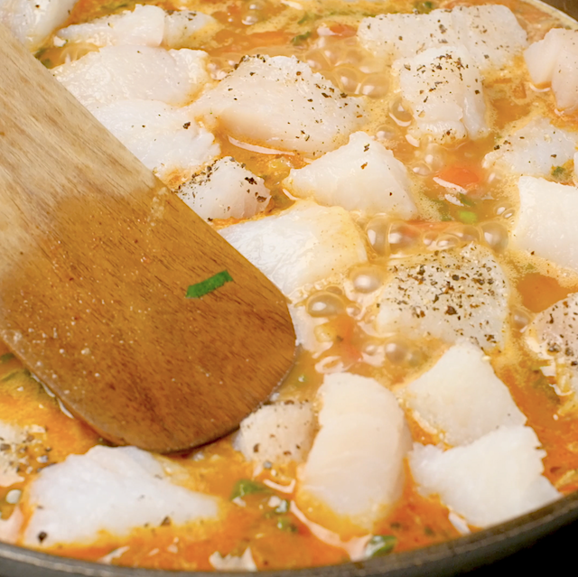 Fish being pressed slightly to submerge in seafood paella broth.