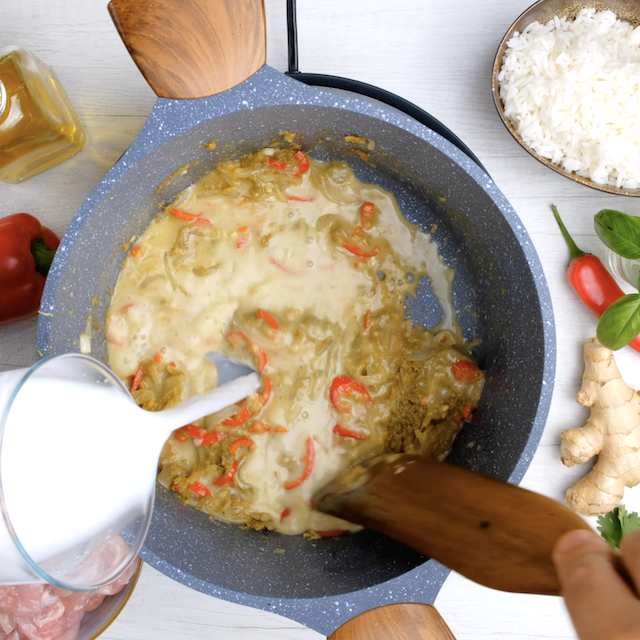 Coconut milk being added to pot to make Thai chicken curry at home.