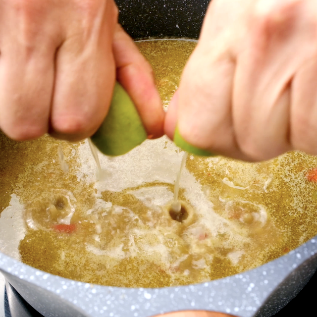 Lime juice being squeezed into a pot with Thai chicken curry.