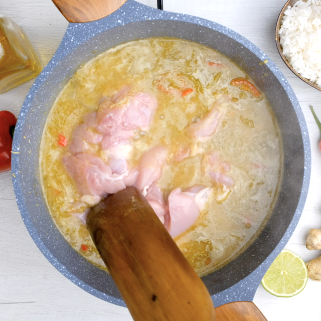 Raw chicken being stirred into Thai chicken curry base in a pot.