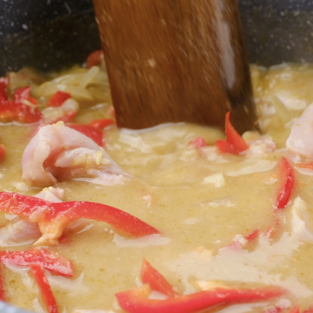 Bell peppers being stirred into Thai chicken curry.