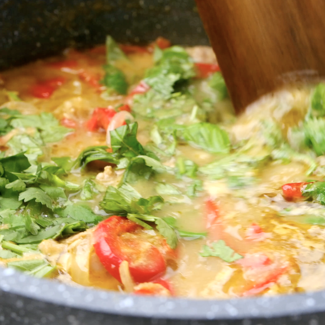 Fresh herbs being stirred into a pot with homemade Thai chicken curry.
