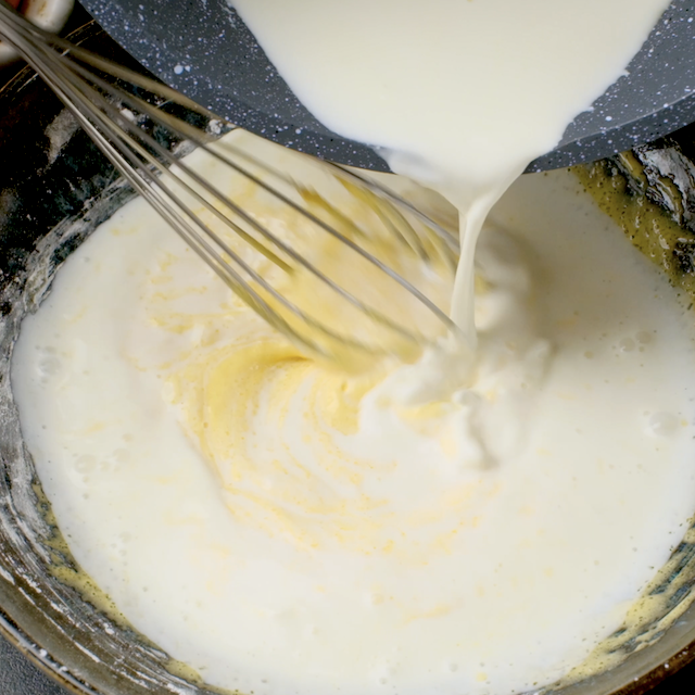 Hot cream being whisked into yolk mixture to make pastry cream for boston cream cupcakes.