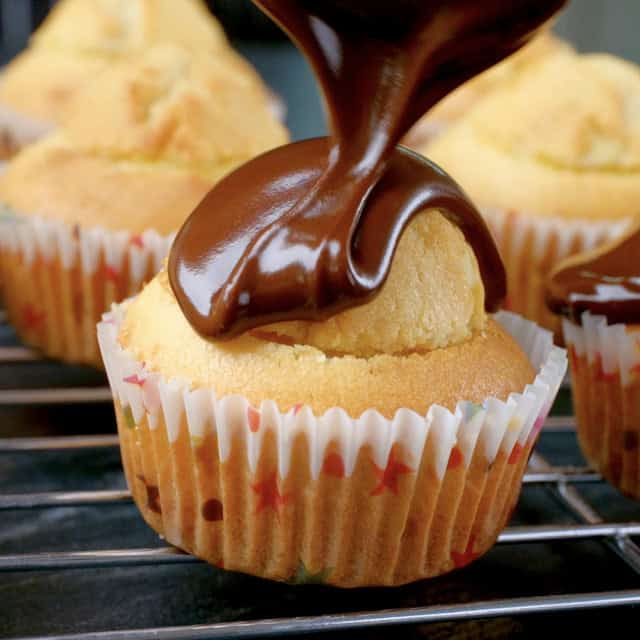 Chocolate glaze being poured on top of cupcake filled with pastry cream to make boston cream cupcakes.
