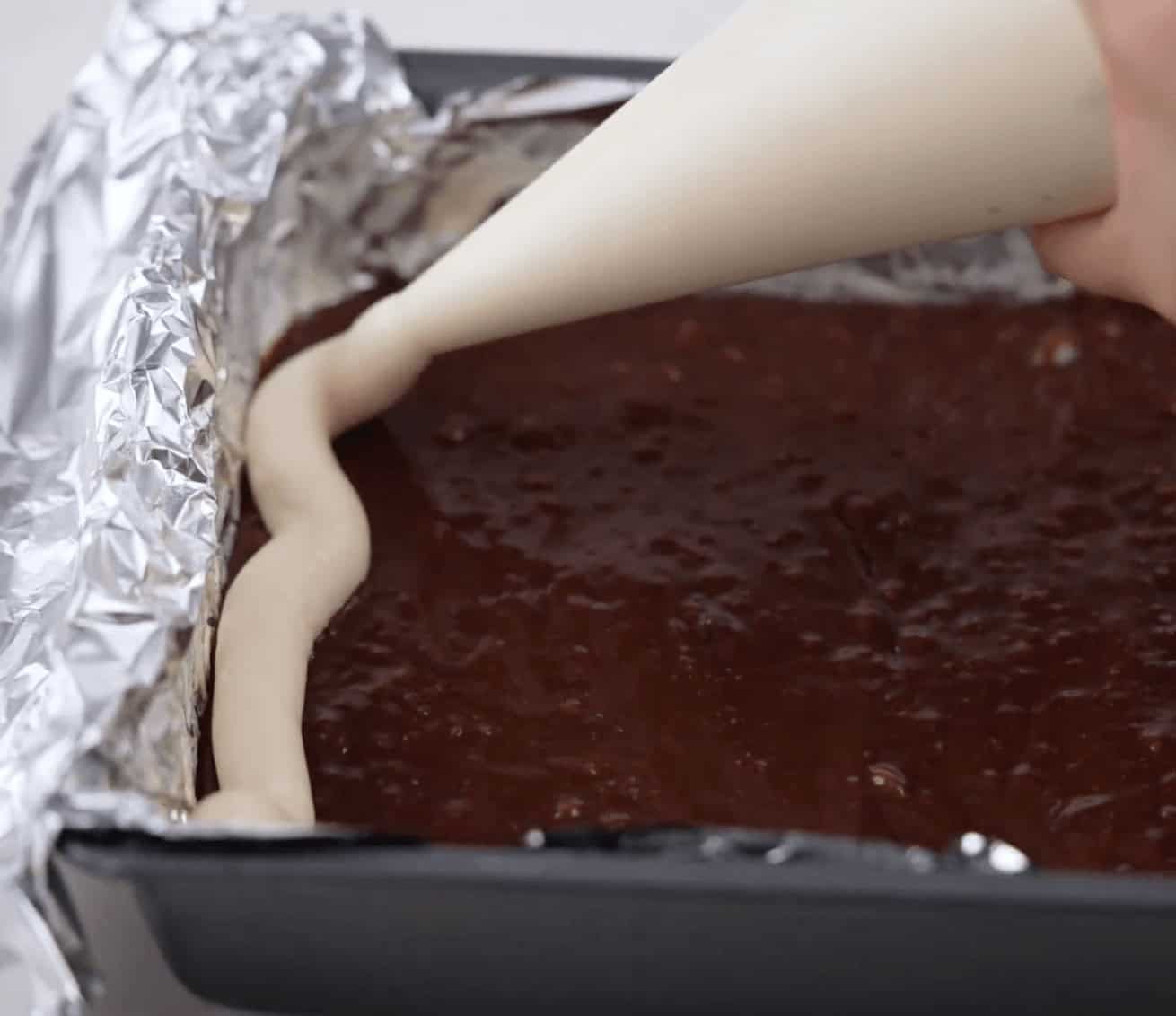 Laying the cheesecake and brownie layers in a pan.