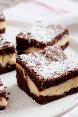 Close up of cheesecake brownie on a white serving plate.