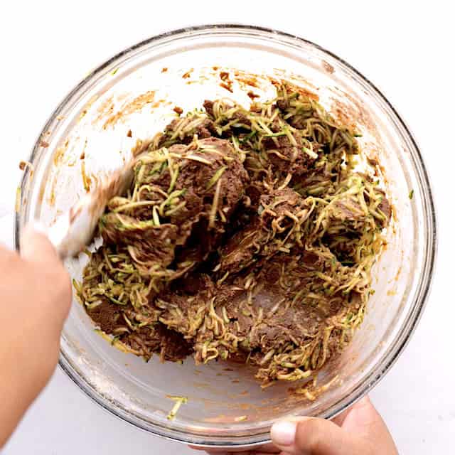 Shredded zucchini being mixed in batter to make chocolate chip zucchini bread.