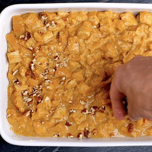 Pumpkin bread pudding mixture being garnished with chopped pecans before baking.
