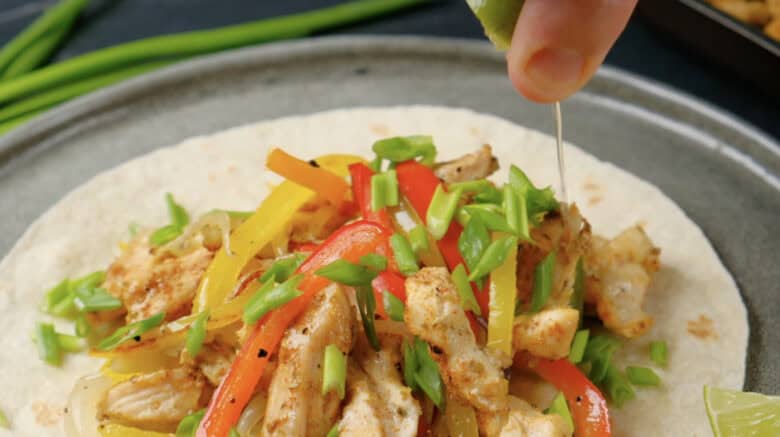 Freshly baked sheet pan chicken fajitas being drizzled with lime juice.