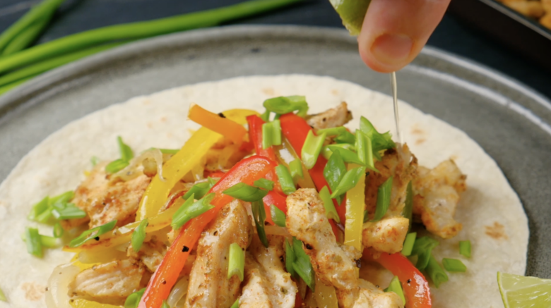 Freshly baked sheet pan chicken fajitas being drizzled with lime juice.