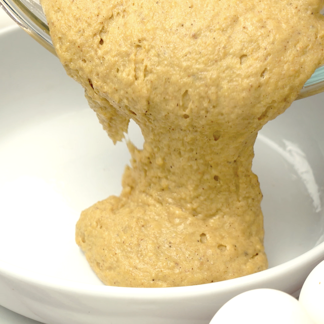 Pumpkin cornbread batter being poured into greased pan.