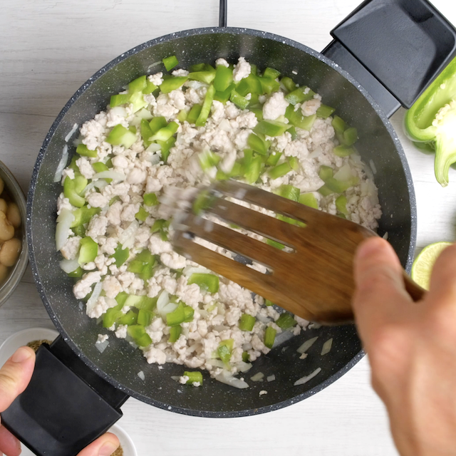 Bell peppers and aromatics being cooked in a pan with ground turkey.