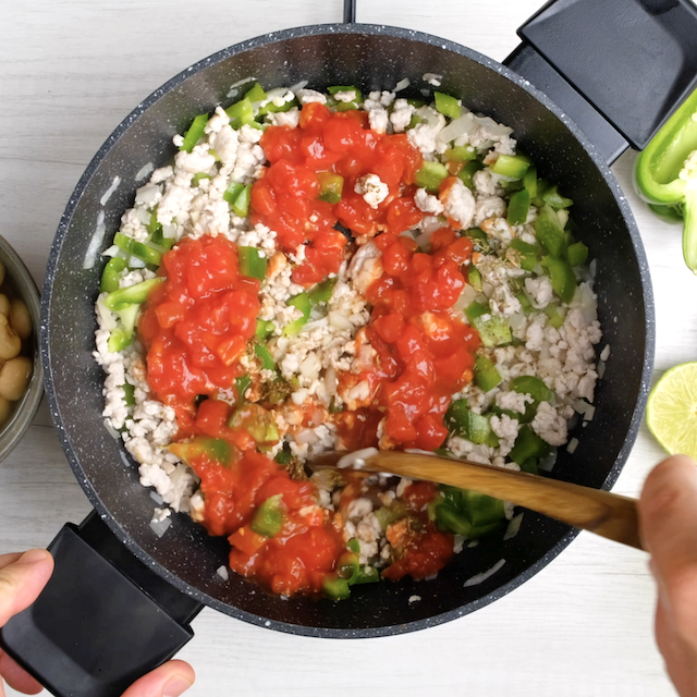 Diced tomatoes and spices added to ground turkey and peppers in a pot.