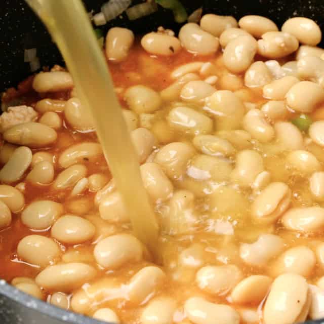 Broth being added to pot with white beans and chili base.