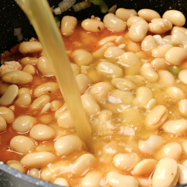 Broth being added to pot with white beans and chili base.